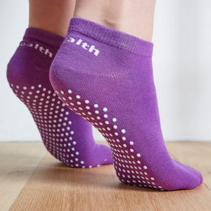Image of Purple Stealth Movement Pilates Grip Sock. The image is taken from the back, with the both feet showing the white grips underneath. The back of the socks say "Stealth.”