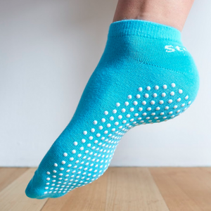 Image of an Aqua Stealth Movement Pilates Grip Sock. The image is taken from the back, with the left foot showing the white grips underneath. The back of the sock says "Stealth.”